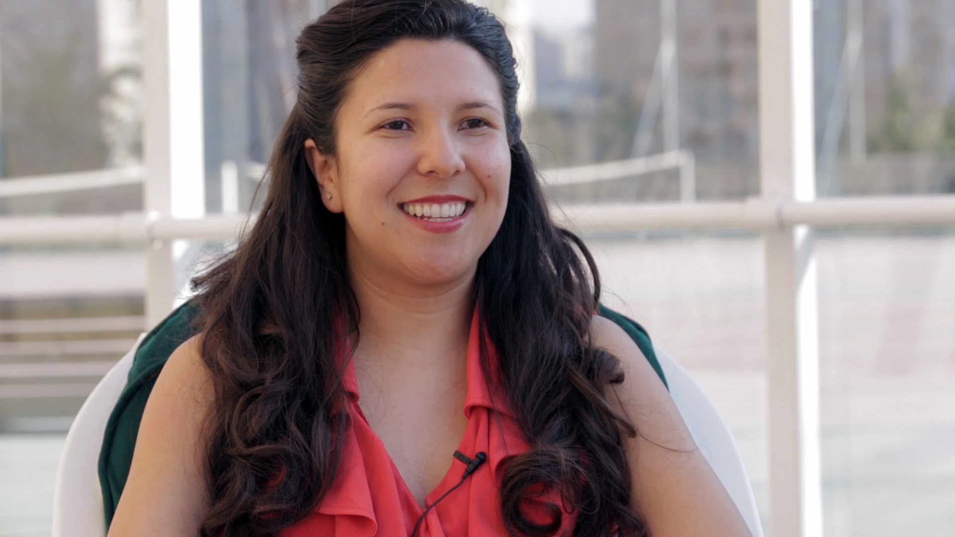 Preview image for the video "Alumni Changemakers: Veronica Palmer" - A closeup of a smiling young woman with long brown hair in a dark pink shirt.
