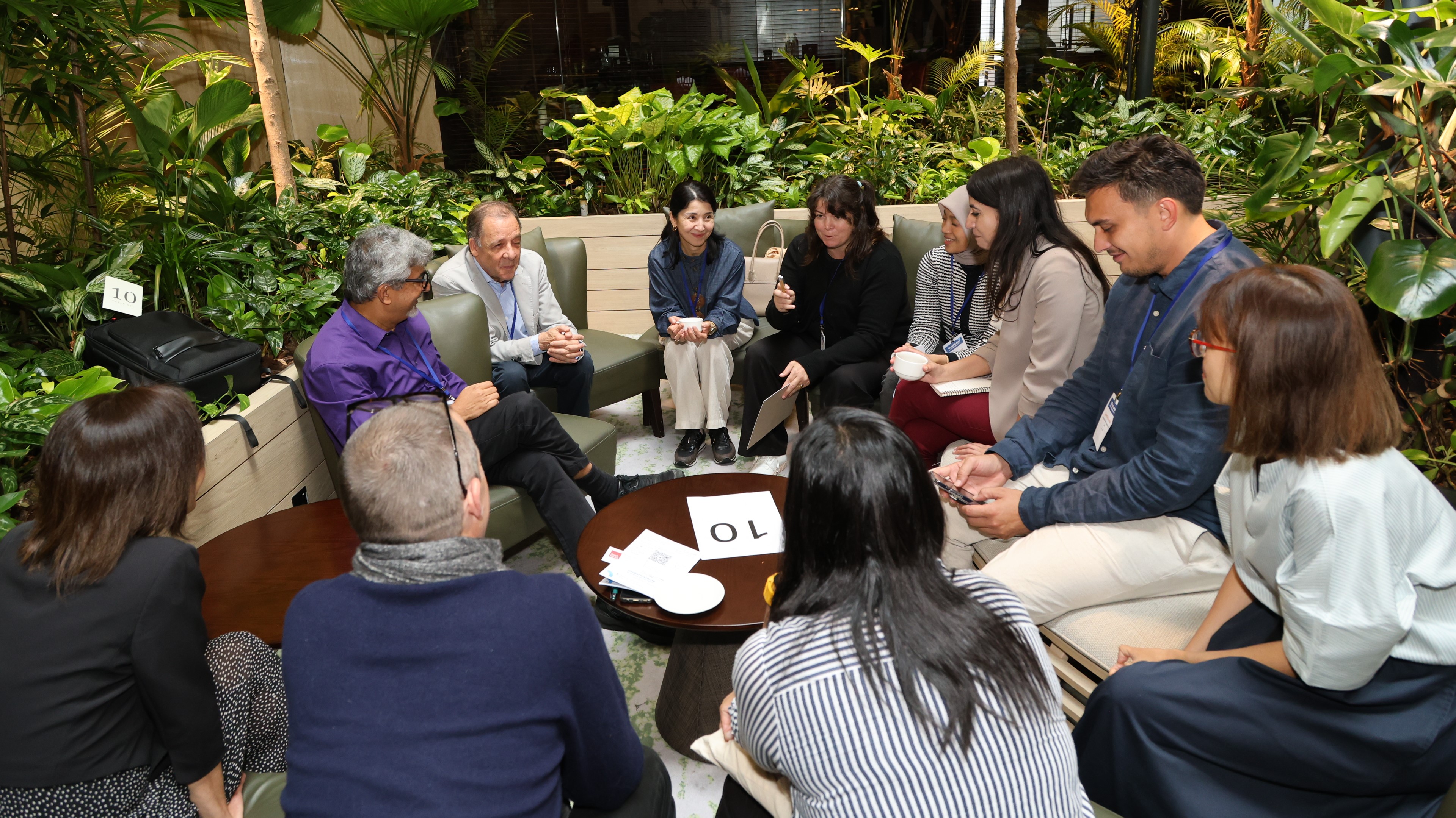 Preview image for the video "Global Forum for Shaping a Better Future - Highlights" - A diverse group of adults sit around a table in conversation.
