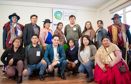 A posed group of 14 adults of all ages, several in traditional Bolivian dress