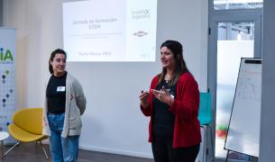 Two young women speak in front of a wall with a projection on it that says "Jornada de Formacion STEM" and includes DOW and Ensena por Argentina logos