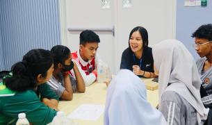 Malaysian students and a woman in a Micron polo shirt have a lively discussion around a table