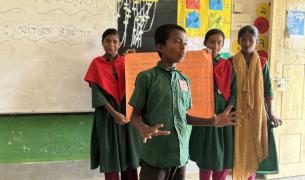 Children hold up a poster and speak in a classroom