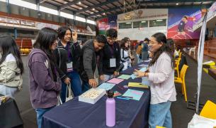 A group of four students stand in front of a desk at a fair talking to the presenter