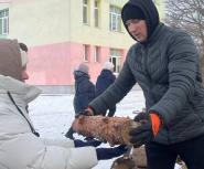 A woman in a black winter jacket and hood hands a log to another person in a light grey winter jacket and hat