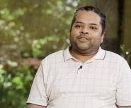 A young African woman in a white shirt and grey sweater stands in the middle of a classroom full of students