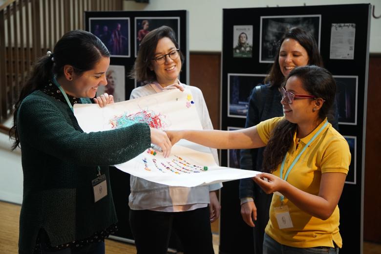 A diverse group of 4 women smile as they collaborate on creating a poster