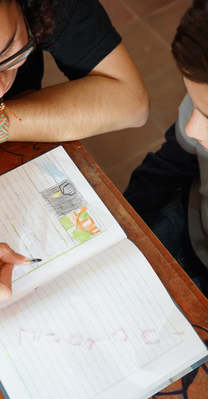 Overhead shot of a teacher and young boy reviewing an entry in a notebook together