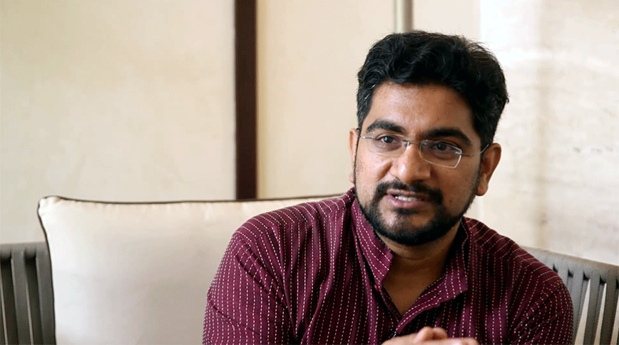 Close up headshot of a young Indian man with a short beard in a maroon shirt