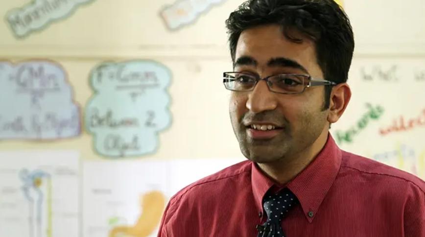 Headshot of a young Indian man with brown hair and glasses in a shirt and tie