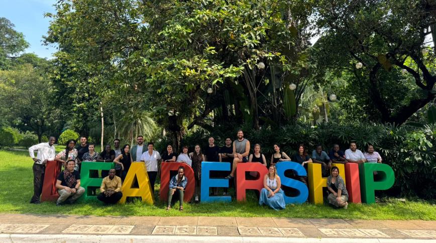 A diverse group of young adults stands around a 3D multi-colored sign that says Leadership