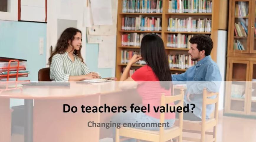 Three young adults, two women with long brown hair and a man, sit around a desk near a bookshelf