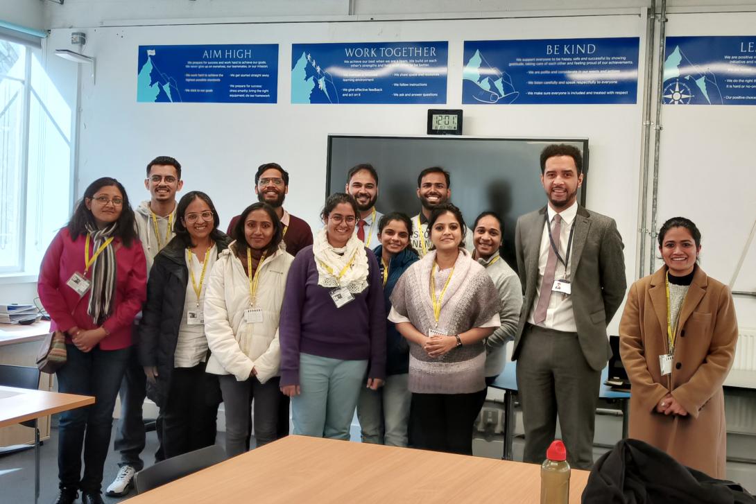 A group of brown-skinned young men and women pose together in front of a classroom