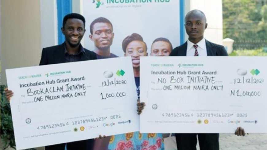 Two young Black men stand holding over-sized award checks