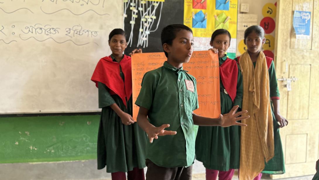 Children hold up a poster and speak in a classroom